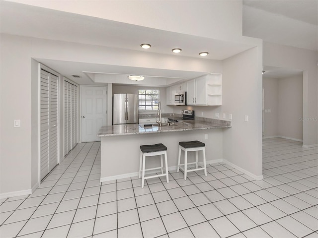 kitchen with kitchen peninsula, stainless steel appliances, white cabinetry, and light stone counters