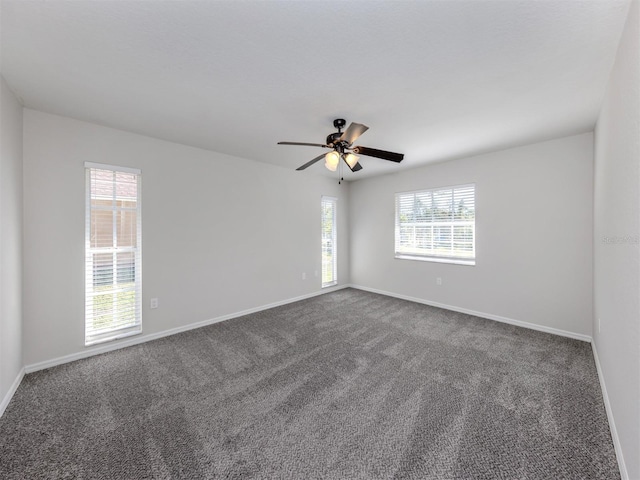 spare room with dark colored carpet, a wealth of natural light, and ceiling fan