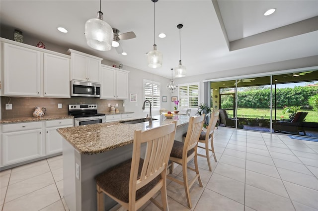 kitchen featuring a kitchen bar, white cabinetry, stainless steel appliances, and a kitchen island with sink