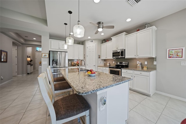 kitchen featuring a kitchen breakfast bar, an island with sink, appliances with stainless steel finishes, light stone counters, and white cabinetry