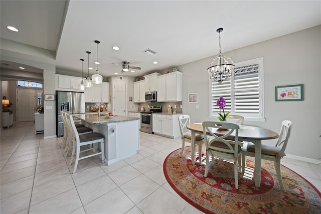 kitchen with white cabinetry, stainless steel appliances, an island with sink, stone countertops, and light tile patterned flooring