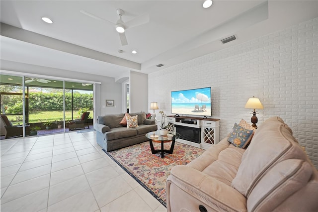 tiled living room with ceiling fan and brick wall