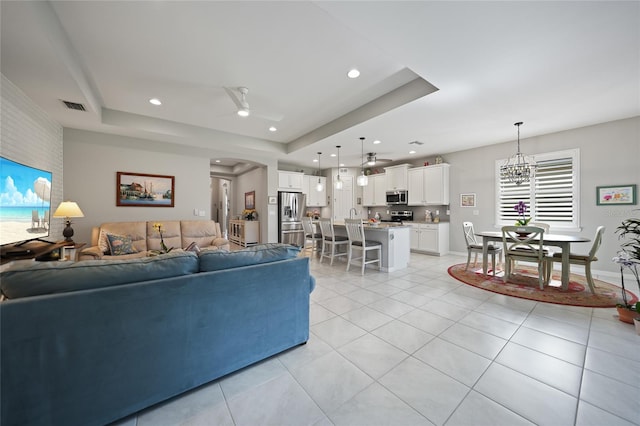 tiled living room featuring ceiling fan with notable chandelier and a raised ceiling