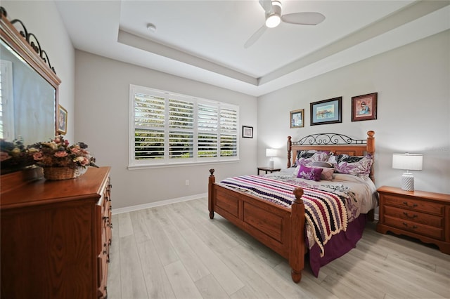 bedroom with a raised ceiling, ceiling fan, and light wood-type flooring