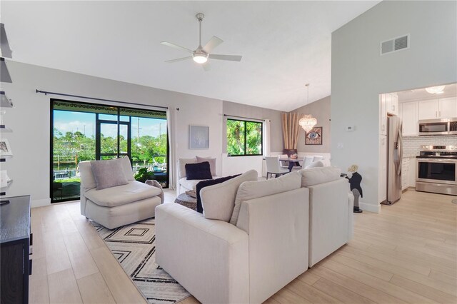 living area featuring visible vents, light wood-style floors, high vaulted ceiling, and ceiling fan with notable chandelier