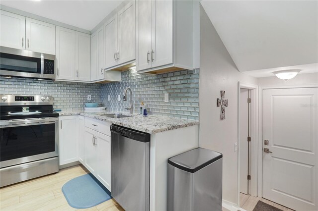 kitchen featuring light stone counters, decorative backsplash, stainless steel appliances, white cabinetry, and a sink