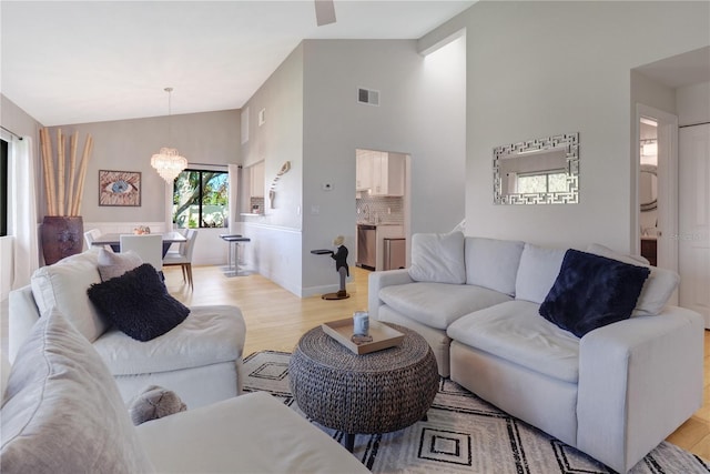 living room with a notable chandelier, visible vents, light wood finished floors, and high vaulted ceiling