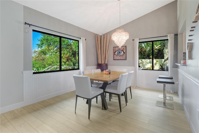 dining space featuring a notable chandelier, a wainscoted wall, light wood-style floors, and lofted ceiling