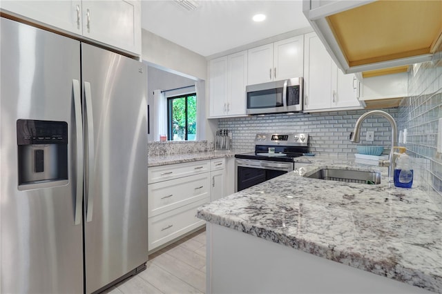 kitchen with light stone countertops, a sink, decorative backsplash, stainless steel appliances, and white cabinetry