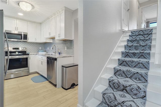 kitchen featuring light stone countertops, light wood-type flooring, decorative backsplash, appliances with stainless steel finishes, and white cabinets