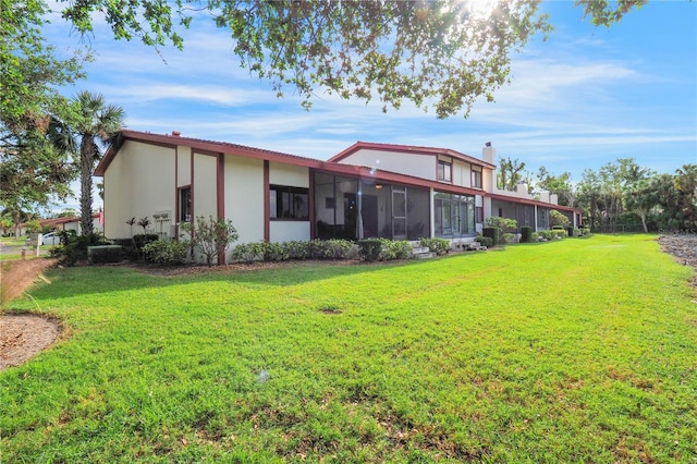 rear view of property featuring stucco siding, a lawn, a chimney, and a sunroom