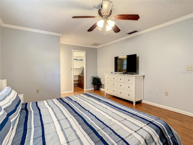 bedroom with a walk in closet, a closet, crown molding, light hardwood / wood-style floors, and ceiling fan