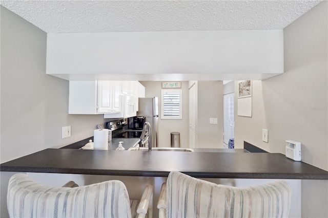 kitchen with white cabinets, a textured ceiling, kitchen peninsula, and black electric range