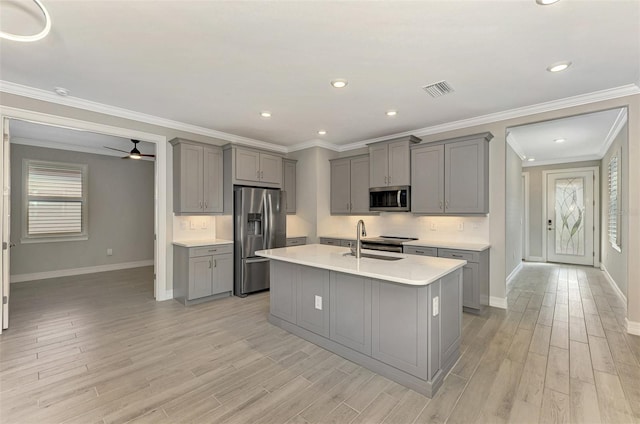 kitchen with gray cabinetry, ceiling fan, stainless steel appliances, a kitchen island with sink, and light wood-type flooring