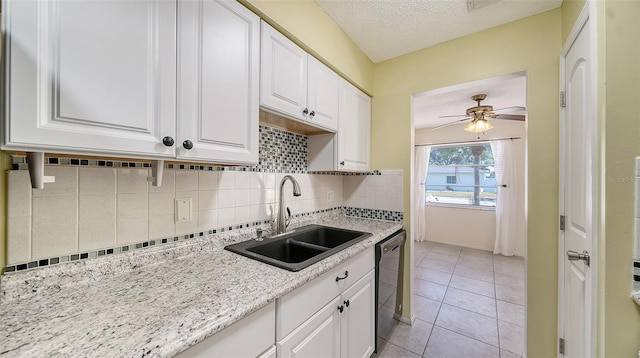 kitchen featuring sink, light tile patterned floors, black dishwasher, a textured ceiling, and white cabinets