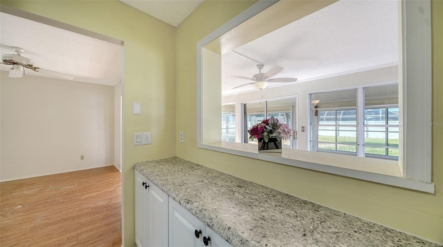 interior space featuring white cabinetry, light stone counters, light hardwood / wood-style floors, and ceiling fan