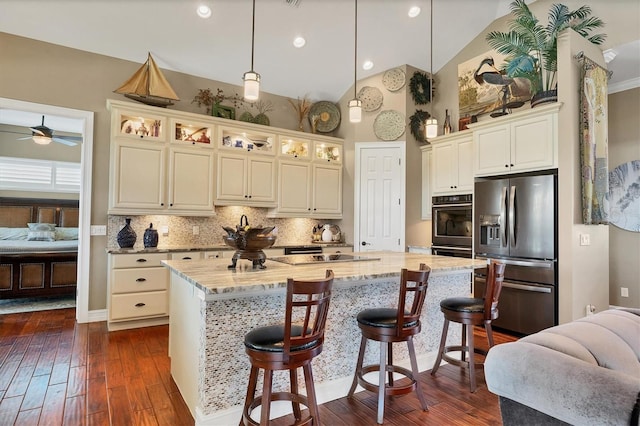 kitchen with light stone countertops, dark hardwood / wood-style flooring, stainless steel appliances, pendant lighting, and an island with sink