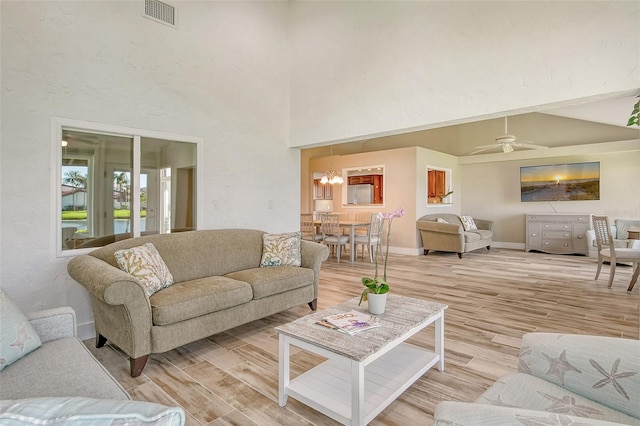 living room featuring light hardwood / wood-style flooring, a high ceiling, and ceiling fan with notable chandelier