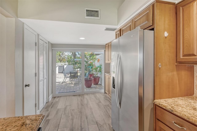 kitchen featuring stainless steel refrigerator with ice dispenser, light wood-type flooring, and light stone counters