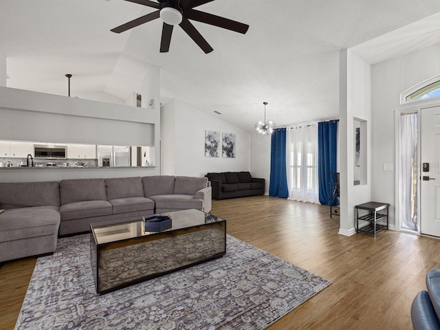 living room with wood-type flooring, ceiling fan with notable chandelier, high vaulted ceiling, and sink