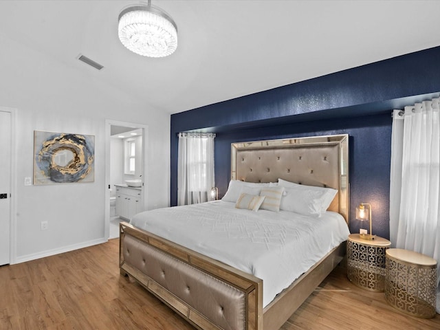 bedroom with connected bathroom, light hardwood / wood-style flooring, vaulted ceiling, and an inviting chandelier