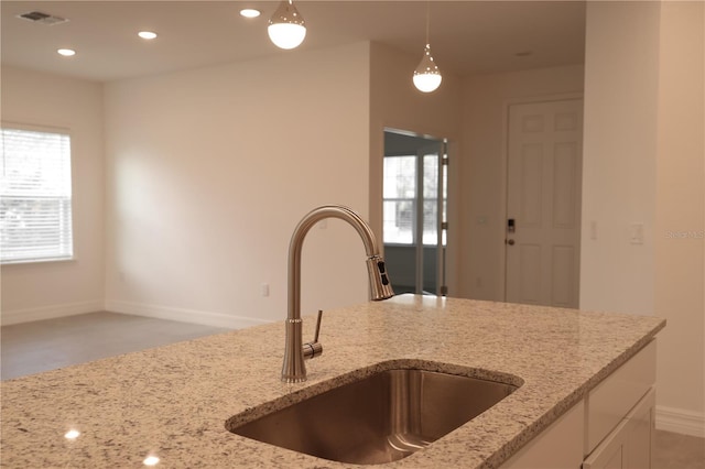 kitchen featuring pendant lighting, white cabinetry, light stone counters, and sink