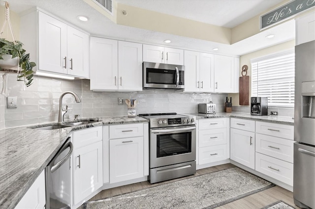 kitchen with white cabinets, appliances with stainless steel finishes, and light stone counters