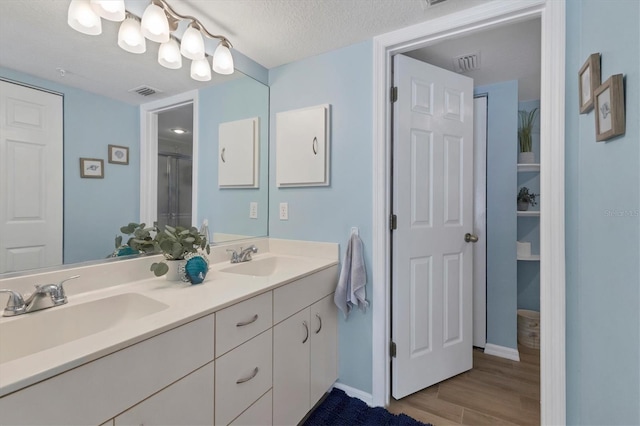 bathroom featuring an enclosed shower, vanity, wood-type flooring, and a textured ceiling