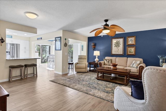 living room with ceiling fan, a textured ceiling, and light wood-type flooring