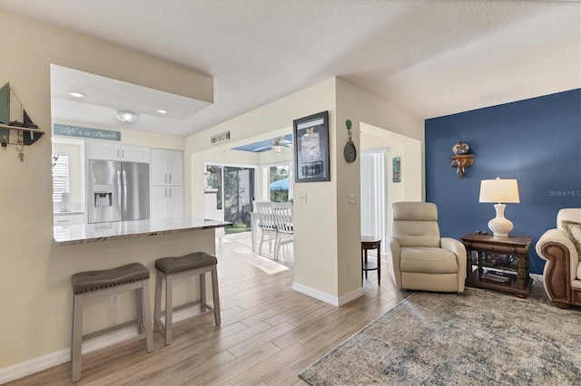815 Montrose Dr Unit 103, Venice, FL 34293 - kitchen with stainless steel fridge with ice dispenser, white cabinets, light stone countertops, a kitchen bar, and light wood-type flooring