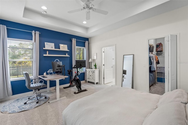 carpeted bedroom featuring a walk in closet, a closet, a raised ceiling, and ceiling fan