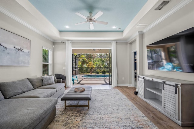 living room with a tray ceiling, ceiling fan, and light hardwood / wood-style floors