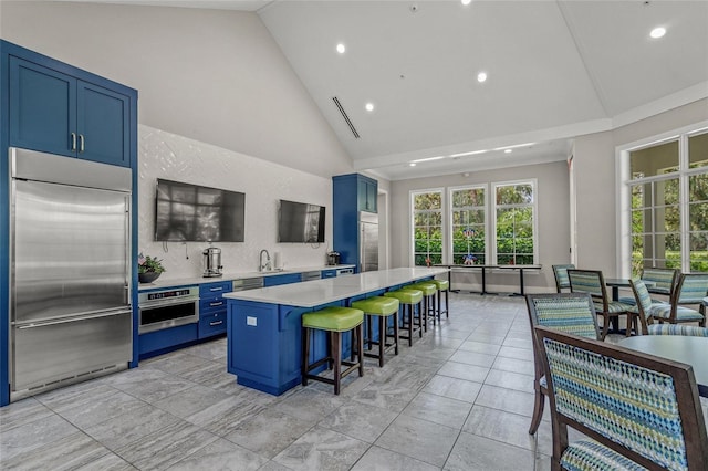 kitchen with blue cabinetry, a center island, high vaulted ceiling, a kitchen bar, and appliances with stainless steel finishes