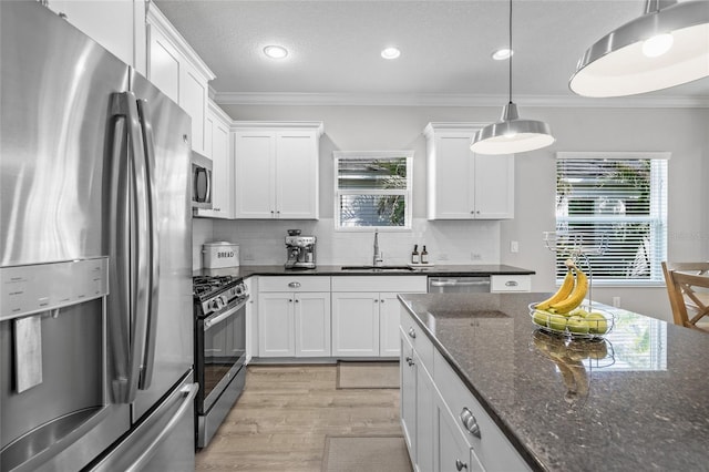 kitchen featuring appliances with stainless steel finishes, dark stone counters, sink, white cabinetry, and hanging light fixtures