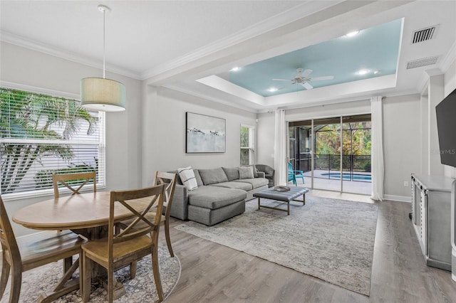 living room featuring a raised ceiling, ceiling fan, crown molding, and hardwood / wood-style flooring