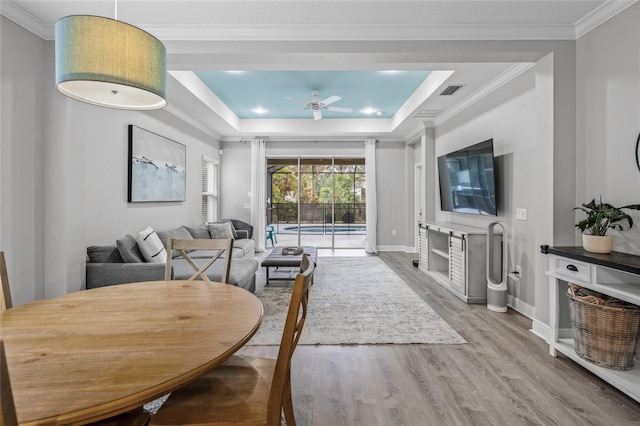 living room with ceiling fan, wood-type flooring, ornamental molding, and a tray ceiling