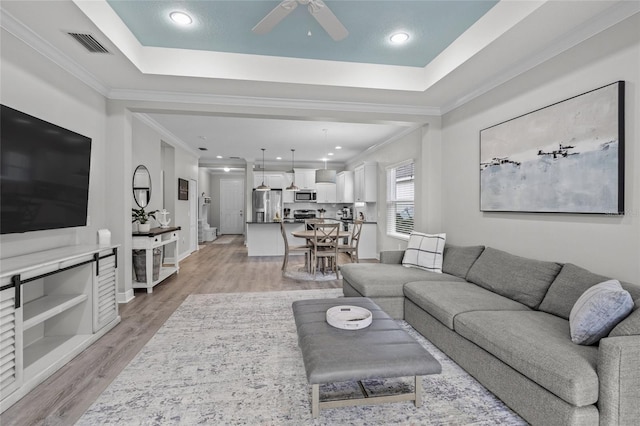 living room with a raised ceiling, light hardwood / wood-style flooring, ceiling fan, and crown molding