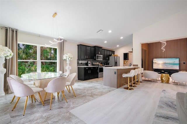 kitchen featuring vaulted ceiling, appliances with stainless steel finishes, tasteful backsplash, decorative light fixtures, and a breakfast bar area