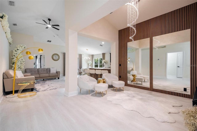 living room with ceiling fan with notable chandelier, light hardwood / wood-style floors, and high vaulted ceiling