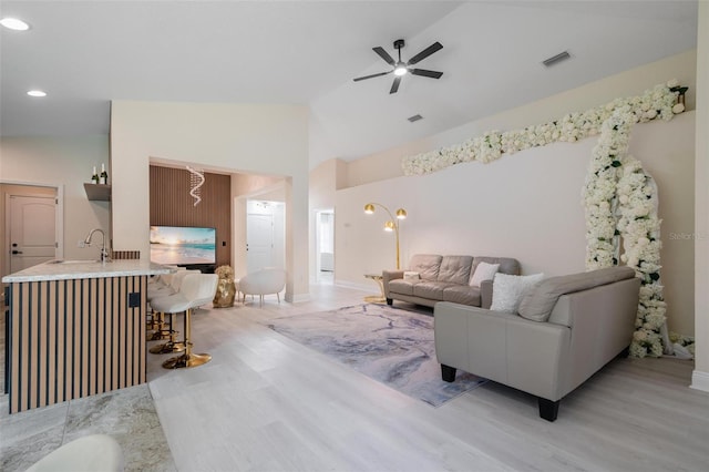 living room with ceiling fan, light wood-type flooring, sink, and high vaulted ceiling