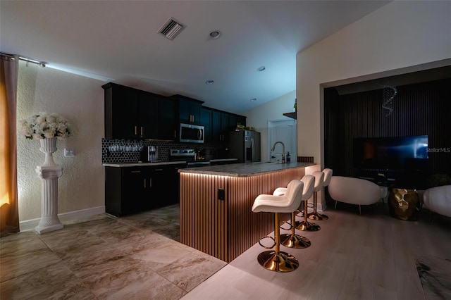 kitchen featuring a kitchen bar, appliances with stainless steel finishes, backsplash, kitchen peninsula, and vaulted ceiling