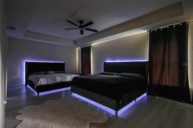 bedroom with wood-type flooring, a tray ceiling, and ceiling fan