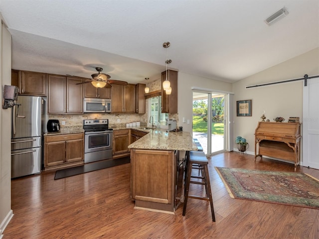 kitchen with pendant lighting, sink, a barn door, kitchen peninsula, and stainless steel appliances