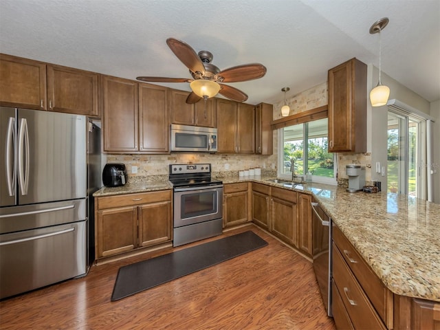 kitchen with kitchen peninsula, appliances with stainless steel finishes, dark hardwood / wood-style flooring, ceiling fan, and decorative light fixtures