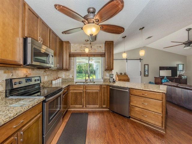 kitchen featuring sink, dark hardwood / wood-style flooring, kitchen peninsula, vaulted ceiling, and appliances with stainless steel finishes