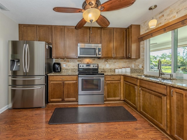 kitchen featuring light stone counters, stainless steel appliances, dark wood-type flooring, sink, and hanging light fixtures