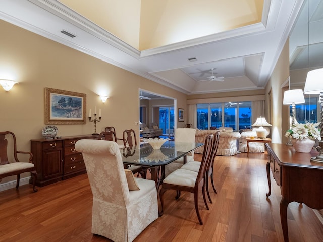 dining space with wood-type flooring, a tray ceiling, ceiling fan, and crown molding