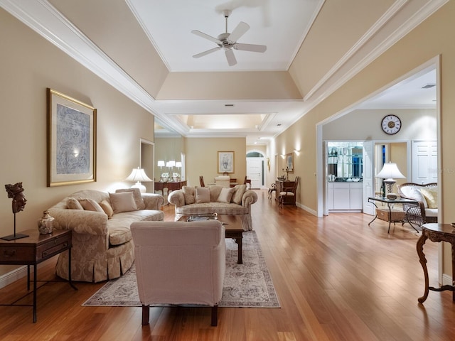 living room featuring a tray ceiling, ceiling fan, light hardwood / wood-style flooring, and ornamental molding