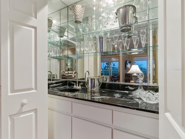 bar with white cabinetry, sink, and dark stone counters