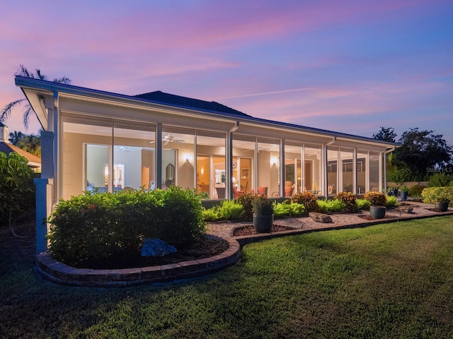 back house at dusk featuring a sunroom and a yard